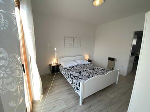 Quarto com cama, mesas de cabeceira e luminária fixada na parede.