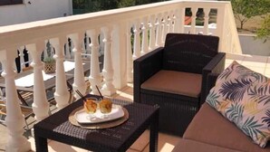 Un balcón con mobiliario de mimbre, una mesa con un plato de comida y una barandilla blanca.