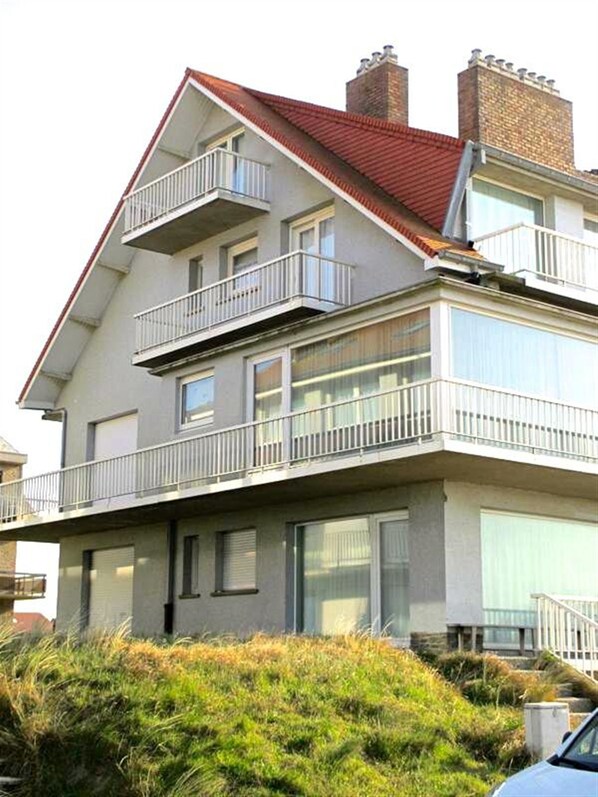 A two-story residential building with a red-tiled roof, white balconies, and large windows.