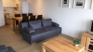 A modern living room with a grey sofa, wooden coffee table, and a dining area with a wooden table and chairs. - Scorpio B 902 (Nieuwpoort)