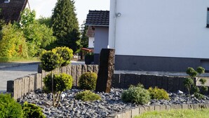 Zona residencial con un edificio blanco, un muro de piedra y diversos arbustos y árboles.