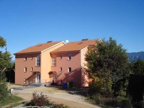 Un bâtiment à deux étages, doté d’un toit recouvert de tuiles rouges, d’une entrée principale avec des marches et d’un petit jardin.