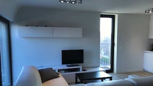 A modern living room with a large sofa, a flat-screen TV, and a small coffee table. There is a sliding glass door leading to a balcony. - Seabreeze 303 (Nieuwpoort)