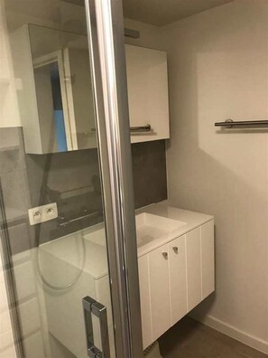 Un baño con cabina de ducha de vidrio, un lavamanos blanco y un espejo sobre el lavamanos.