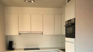 A compact kitchen with white cabinets, a built-in oven, and a coffee maker on the countertop. - Seabreeze 303 (Nieuwpoort)