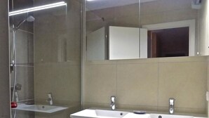 Un baño con ducha a nivel de suelo, dos lavamanos y un espejo grande.