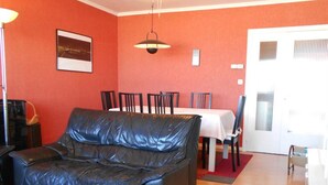 Una sala de estar con un sofá de cuero negro, una mesa de comedor con sillas, una pared roja y una puerta blanca.