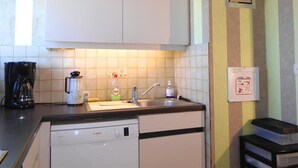 Una cocina compacta con armarios blancos, un lavavajillas Bosch, una cafetera y un fregadero.