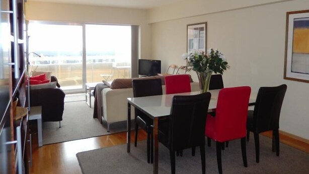 A modern living room with a dining area, large windows, and a flat-screen TV. - Marco Polo 0102 (Nieuwpoort)