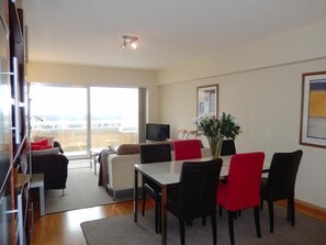 A modern living room with a dining area, large windows, and a flat-screen TV. - Marco Polo 0102 (Nieuwpoort)