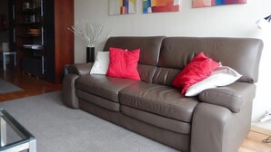A modern living room with a brown leather sofa, red and white cushions, and abstract art on the wall. - Marco Polo 0102 (Nieuwpoort)