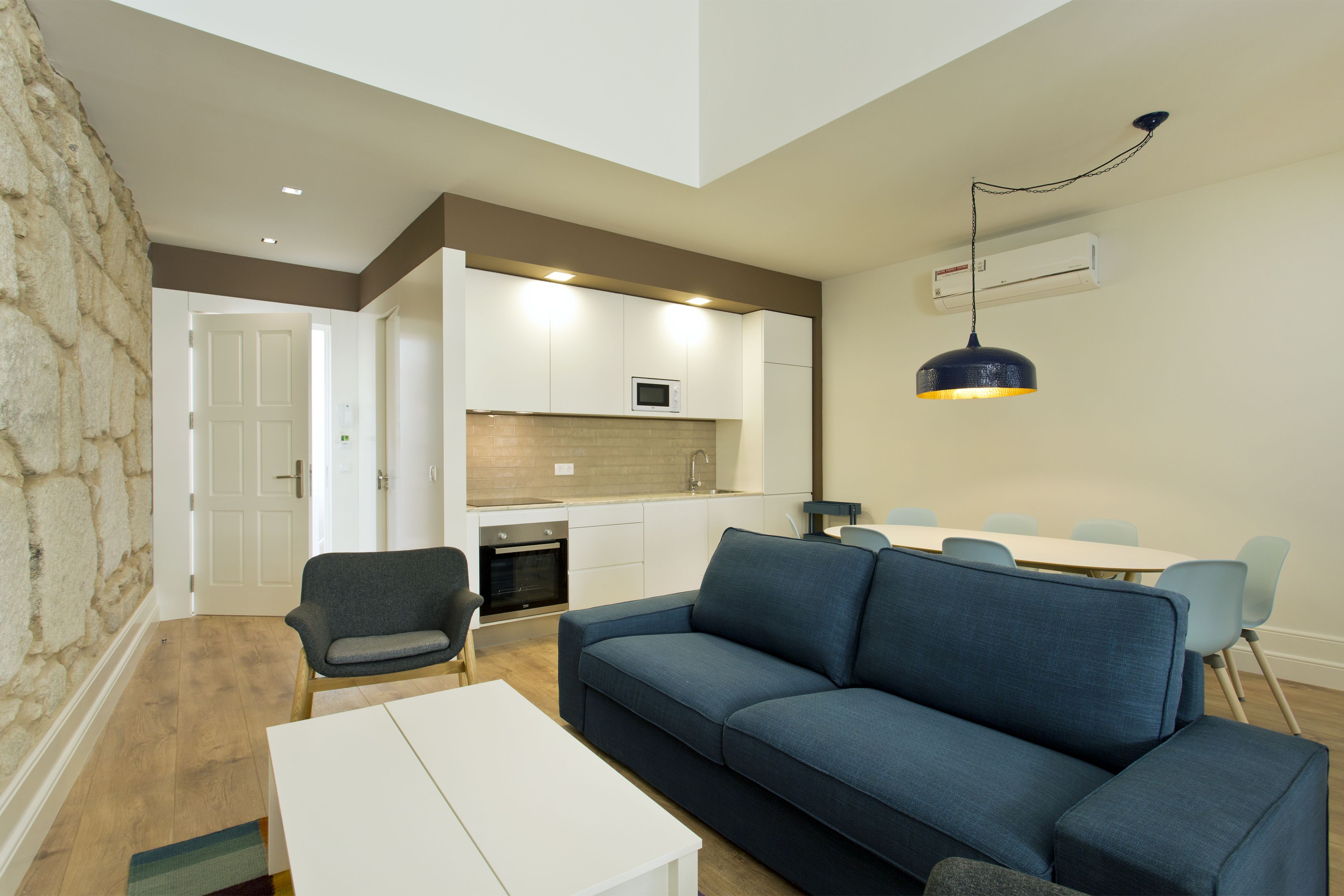 A modern living room with a blue sofa, a white coffee table, and a stone accent wall.