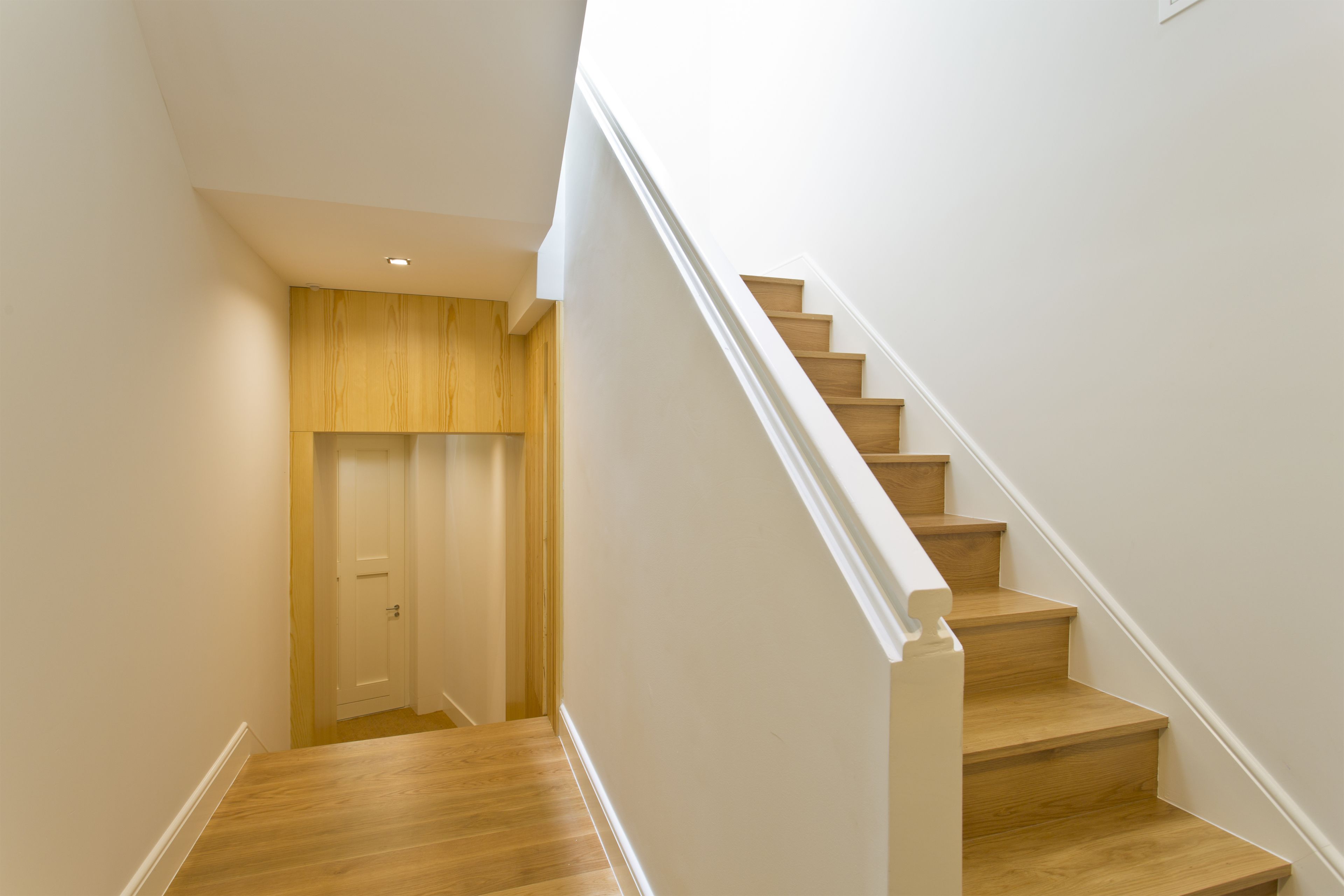 A staircase with wooden steps and white railings, leading to a door with a wooden panel wall.