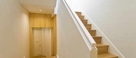 A staircase with wooden steps and white railings, leading to a door with a wooden panel wall.