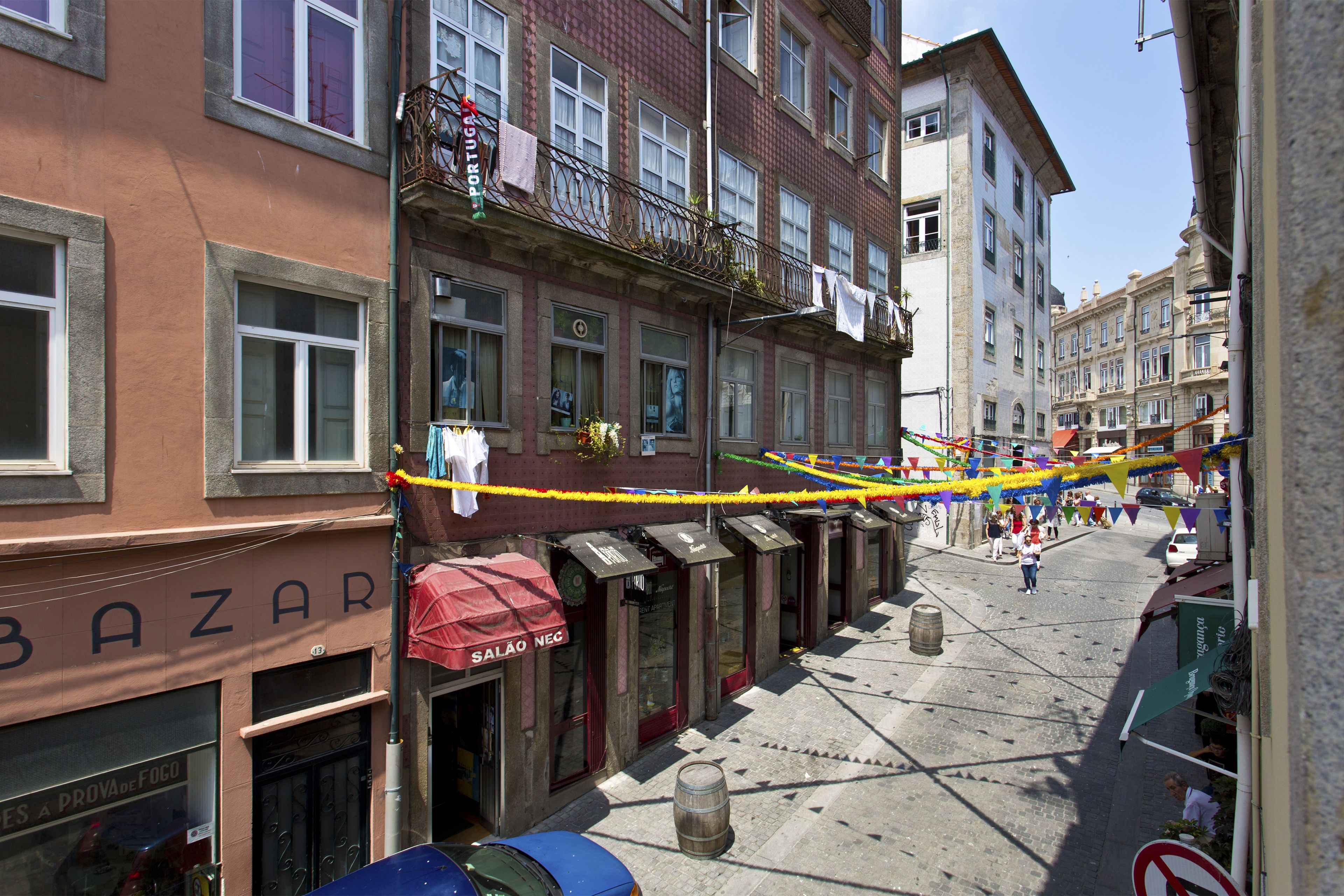 A street with buildings, a blue car, and a wooden barrel.
