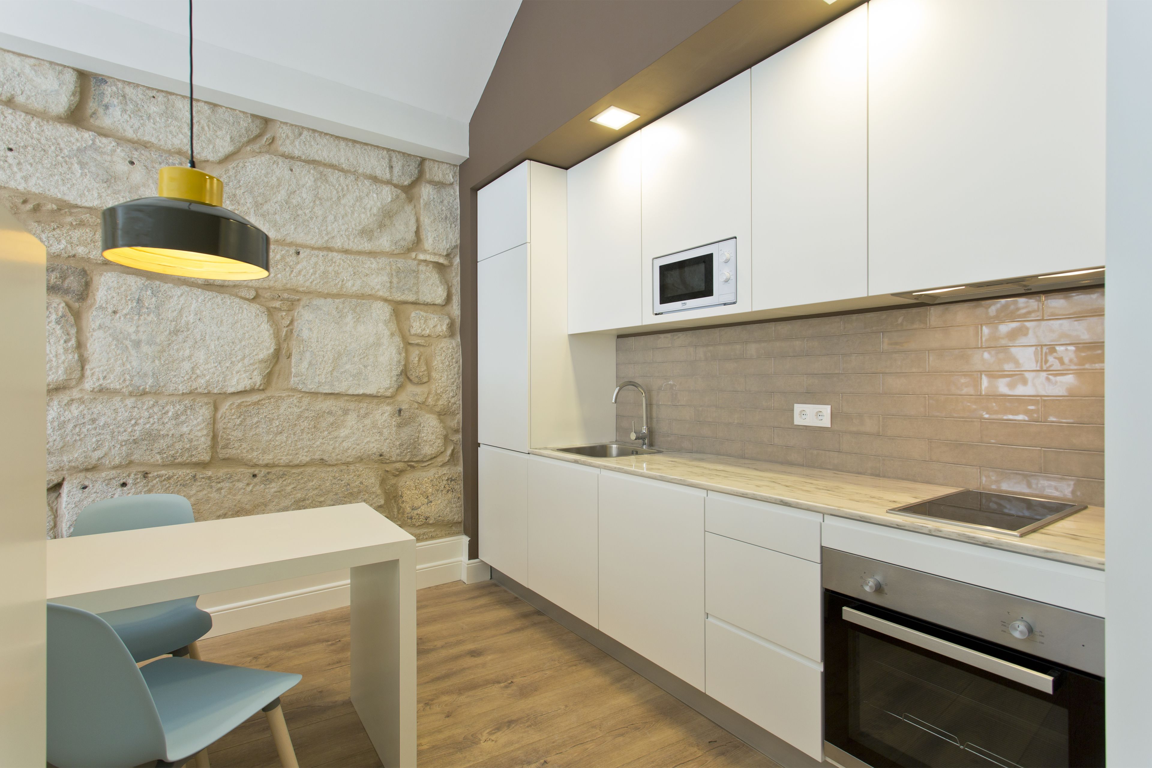 A modern kitchen with white cabinets, a stone accent wall, a built-in microwave, and a wooden countertop.
