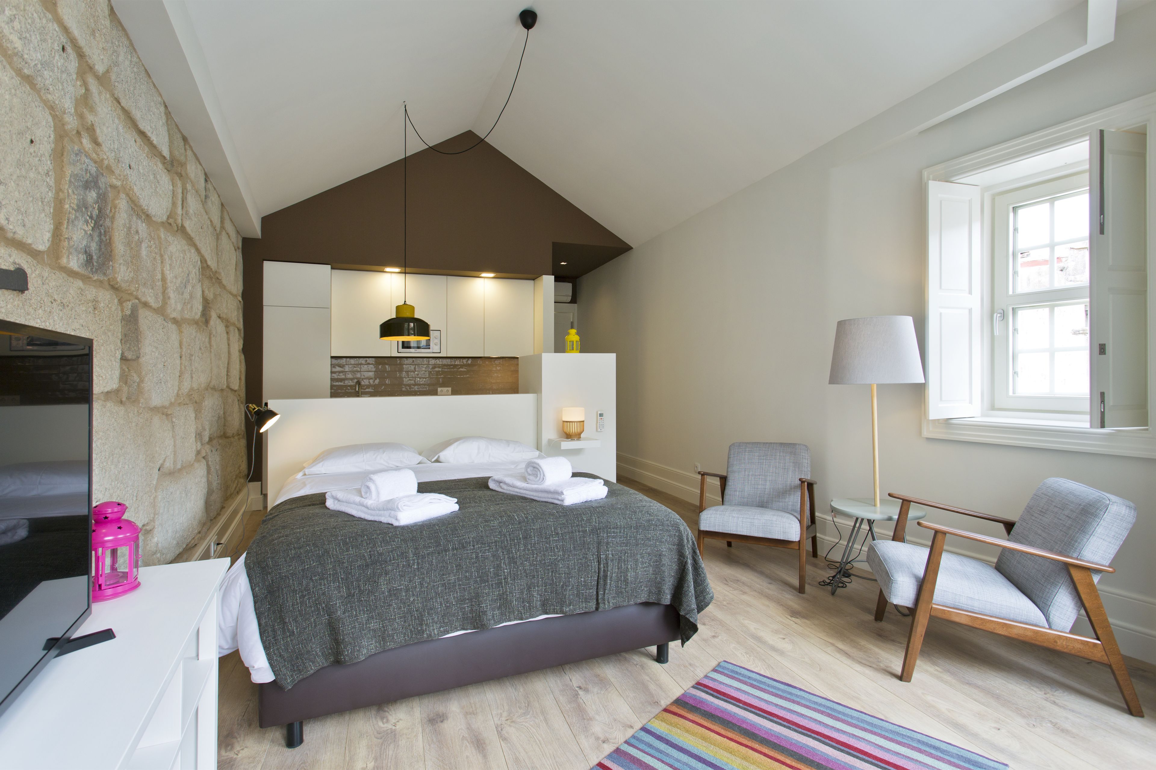 A bedroom with a bed, a desk, a chair, a lamp, and a window.