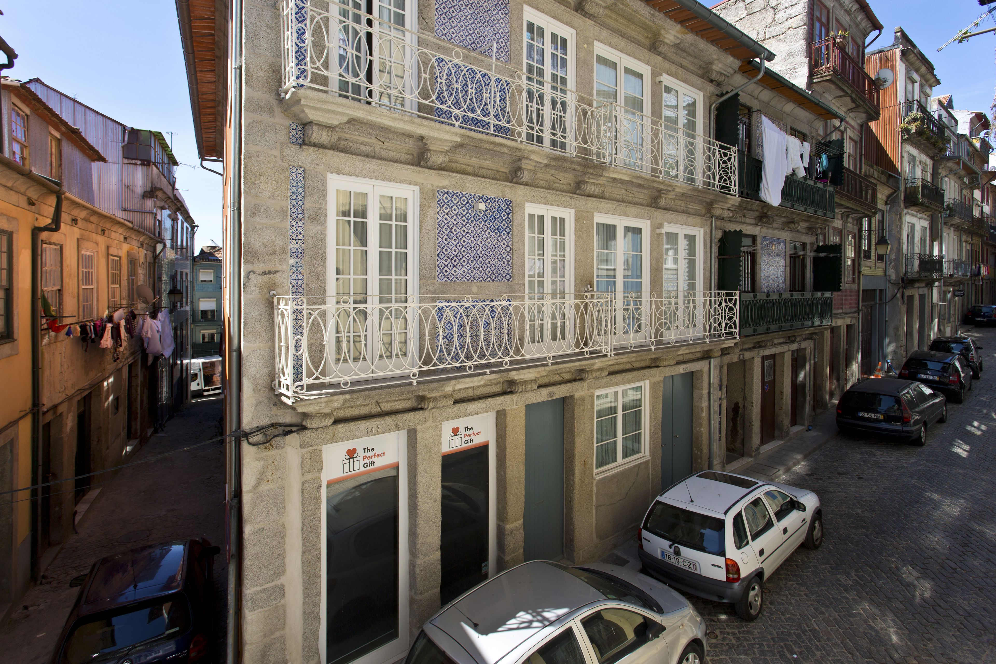 A multi-story building with a balcony, a shop on the ground floor, and parked cars on the street.