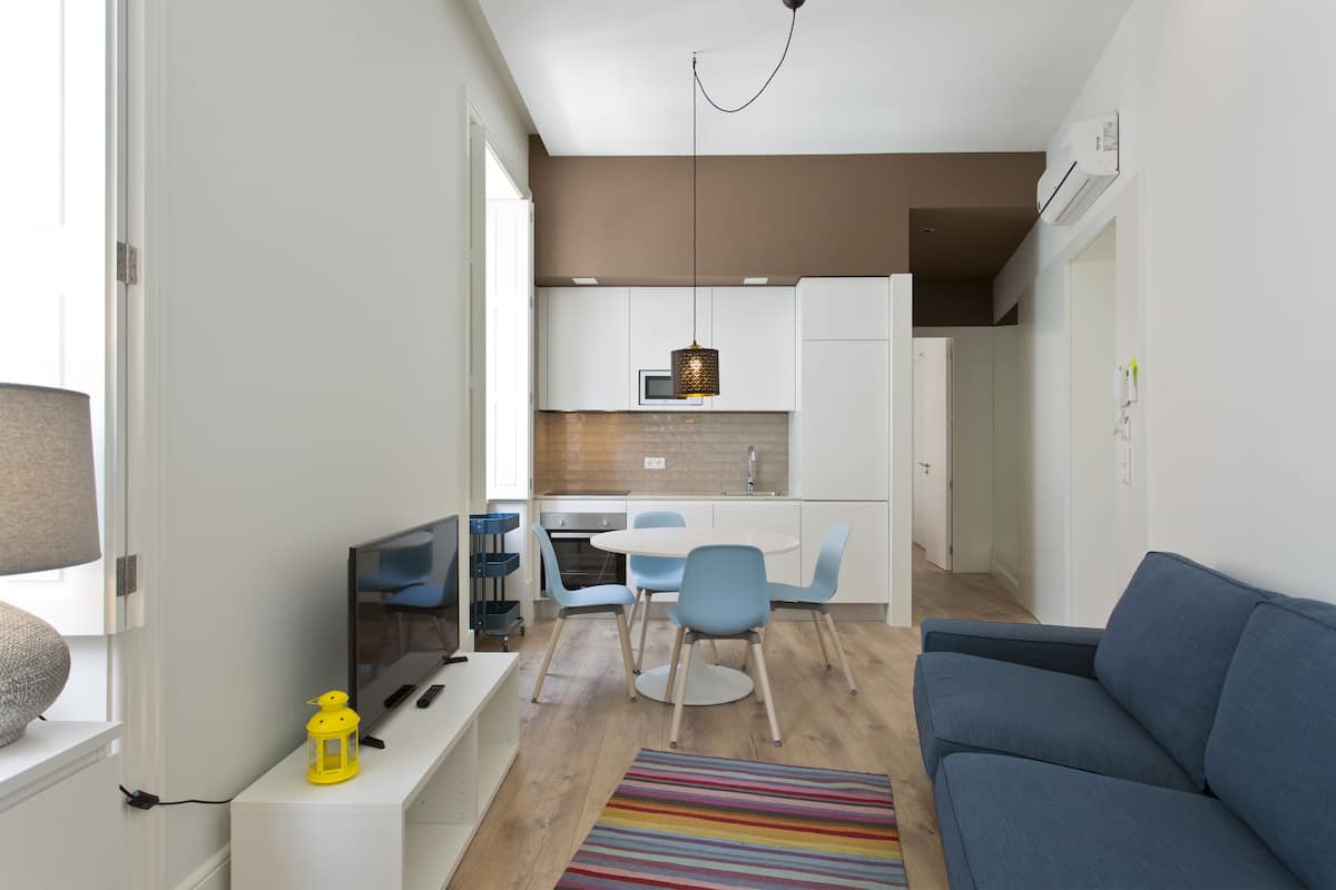 A modern apartment with a living room, kitchen, and dining area. It includes a blue sofa, a dining table with chairs, and a TV.