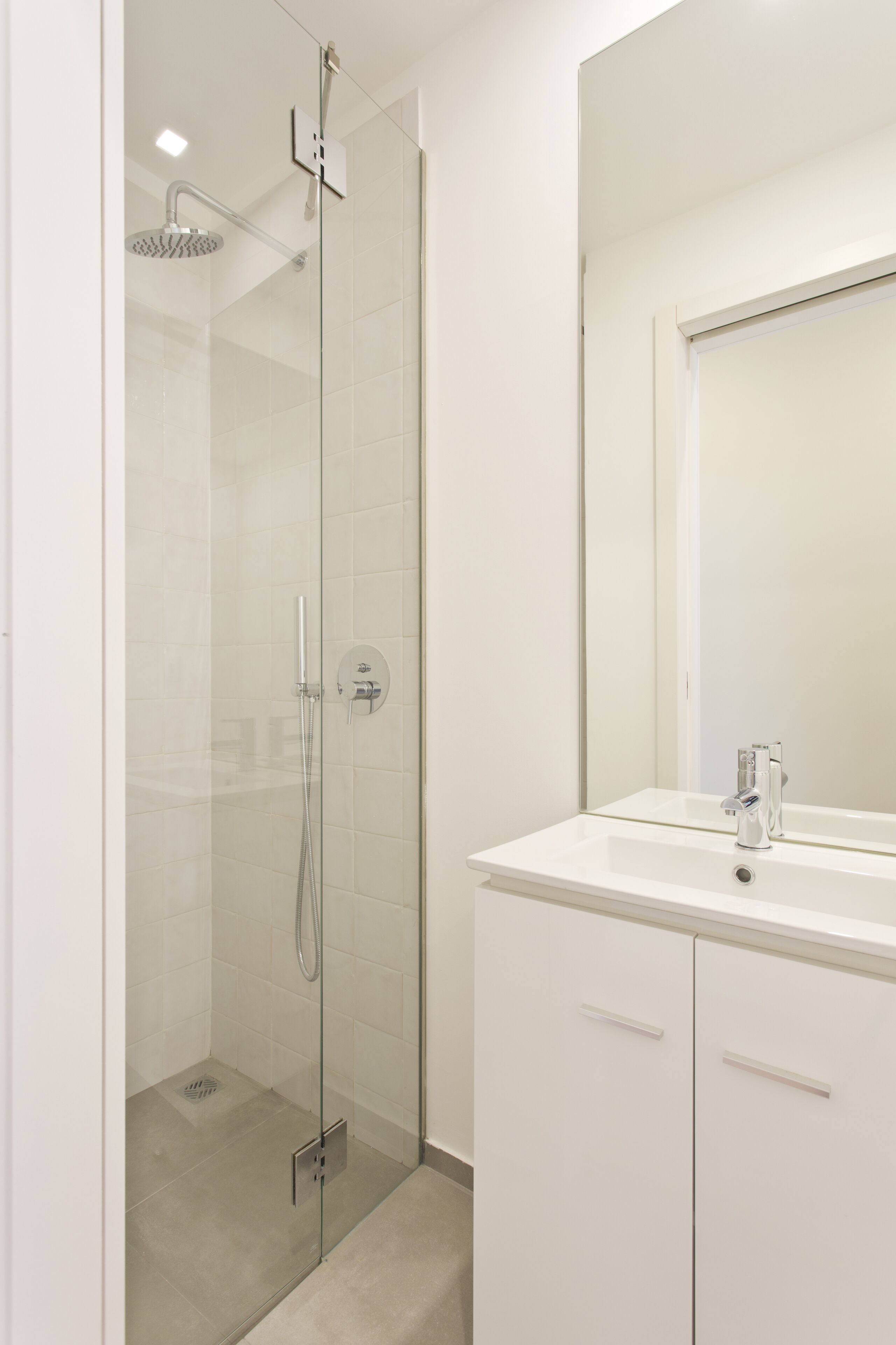 A modern bathroom with a glass-enclosed shower, a white sink, and a large mirror.
