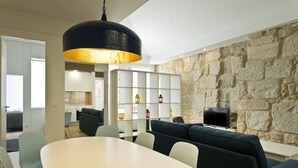 Una sala de estar moderna con una pared de piedra, una lámpara colgante negra grande, una mesa de comedor blanca y un sofá.