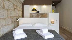 Un moderno cuarto de hotel con pared de acento de piedra, una cama con toallas blancas dobladas con esmero, una lámpara colgante y una mesita de noche pequeña con lámpara.