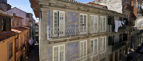 Um edifício de vários andares com varandas, uma placa indicando um comércio local e uma rua de calçada.