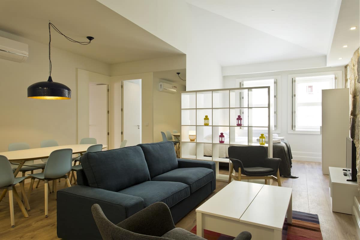 A modern living room with a sofa, chairs, a dining table, and a bookshelf.