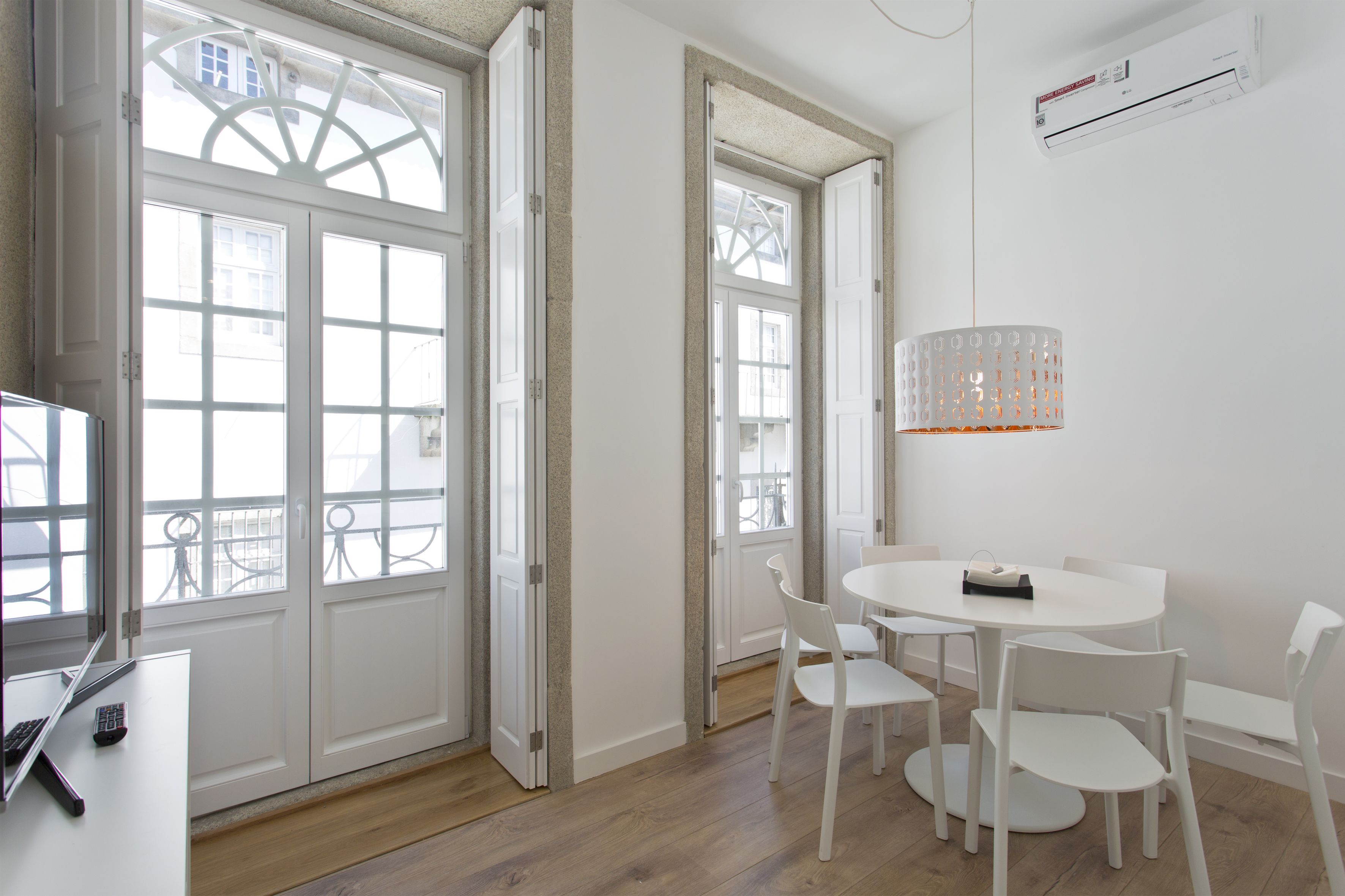 A modern room with a white interior, a round dining table with chairs, a large window with a view, and an air conditioning unit on the wall.