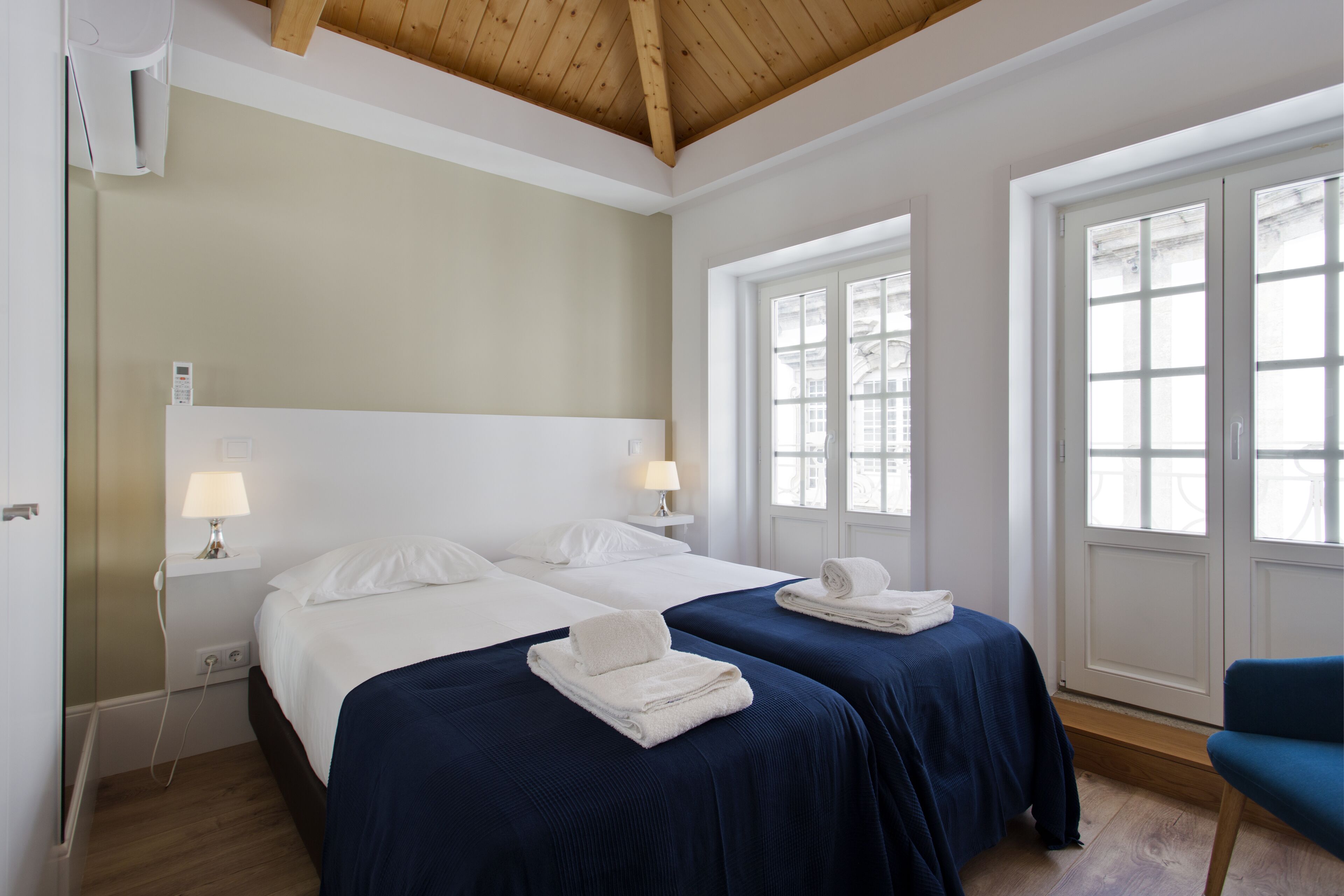 Een hotelkamer met twee bedden, een houten plafond, een raam met uitzicht en een stoel.
