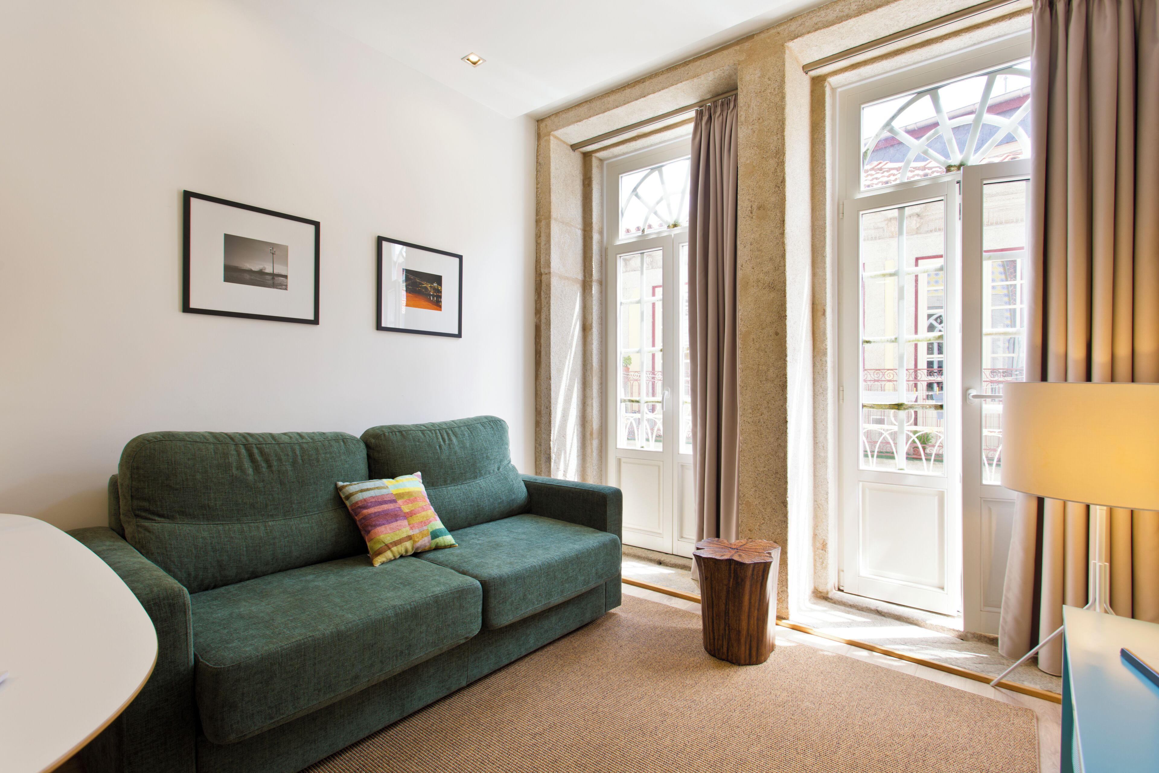 A room with a green sofa, a small round table, two framed pictures on the wall, and a window with curtains.