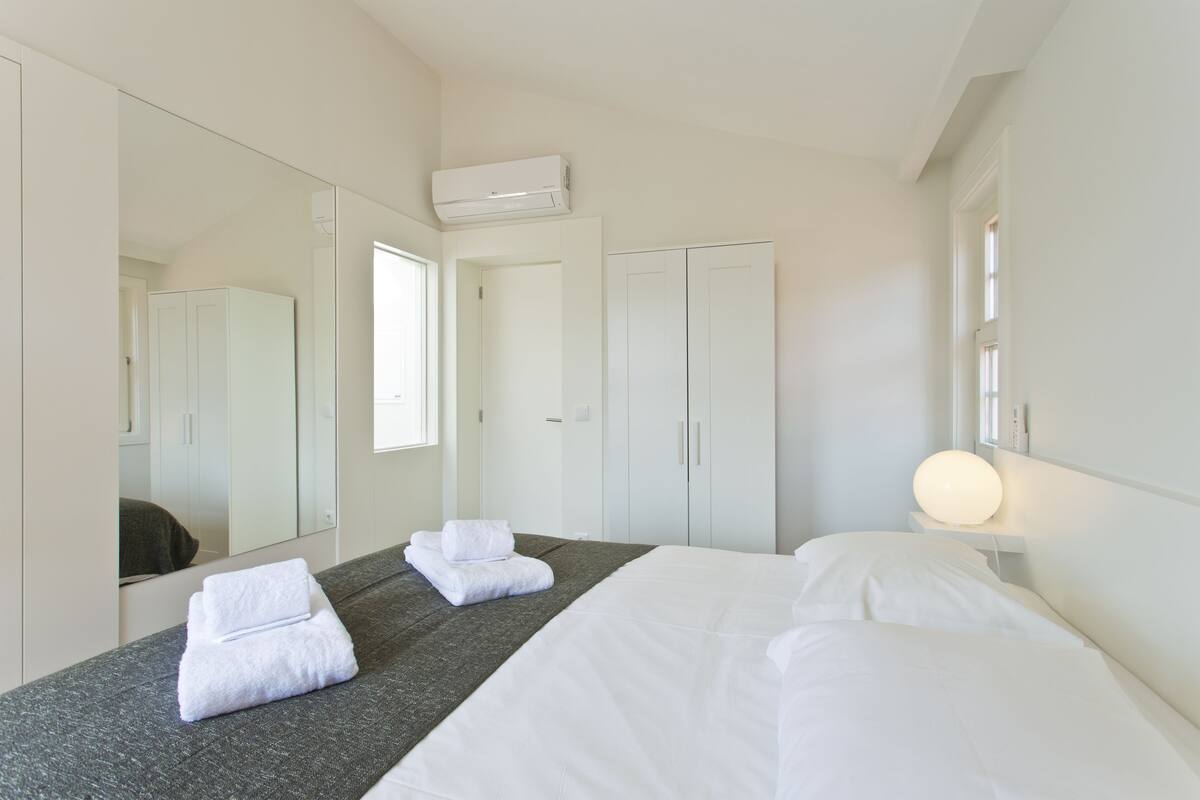 A hotel room with a bed, a large mirror, a wardrobe, and a bedside lamp.