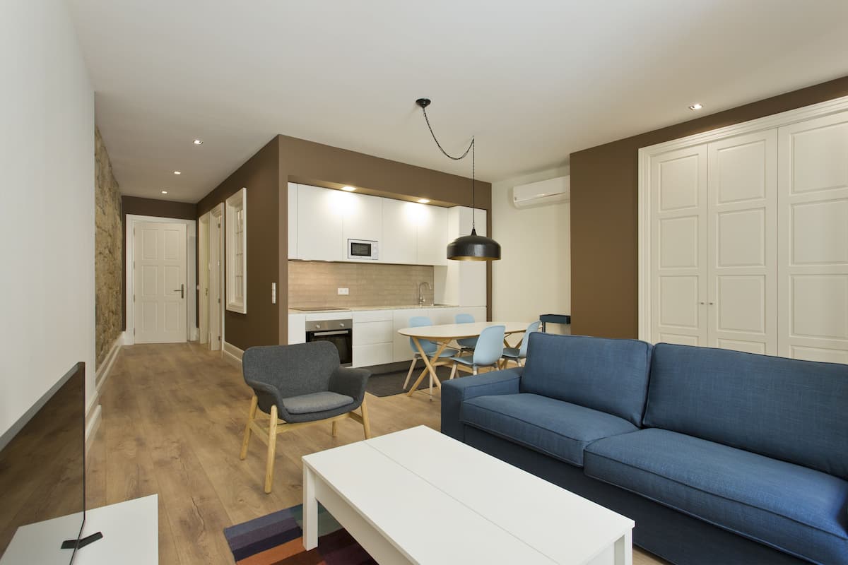 A modern living room with a blue sofa, a white coffee table, and a dining area with a table and chairs.