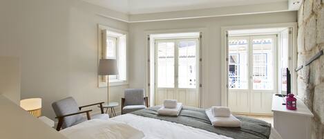 A hotel room with a large bed, two chairs, a desk, and a stone accent wall.