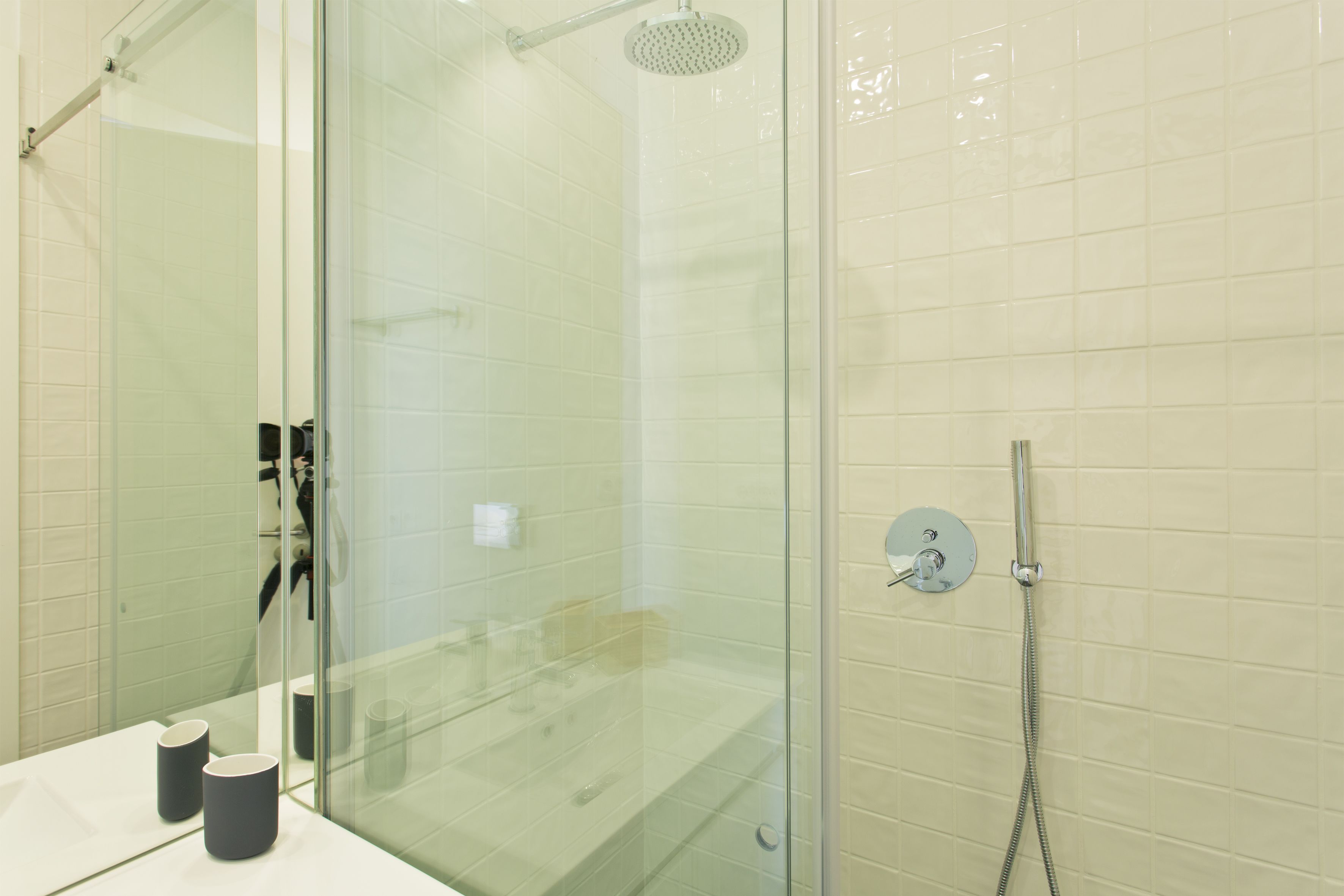 A modern bathroom with a glass shower enclosure, a white tiled wall, and a visible showerhead.