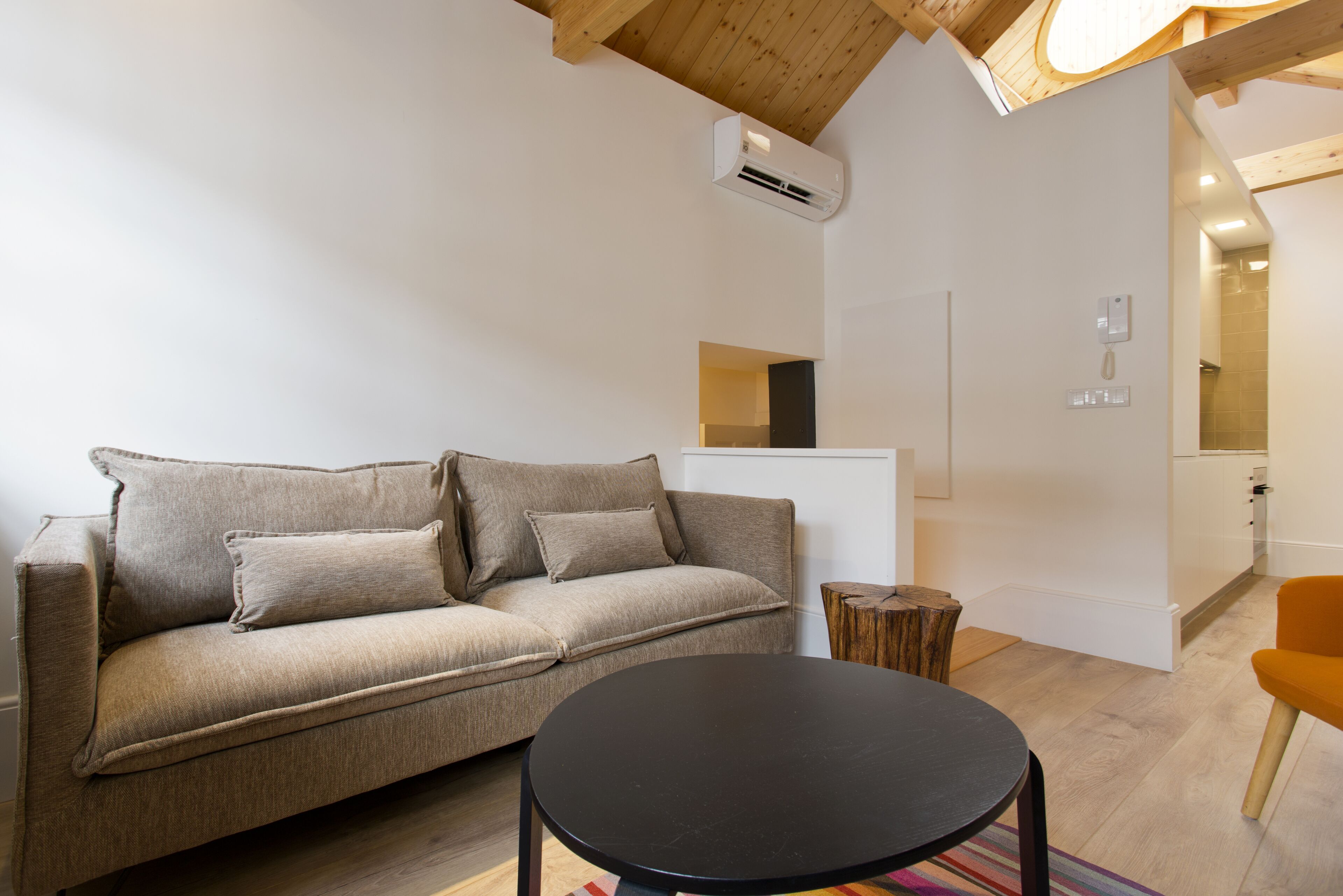A modern living room with a beige sofa, a black coffee table, and a wooden ceiling.