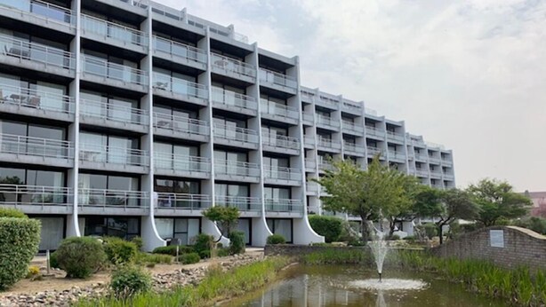 A modern multi-story building with balconies, a small pond with a fountain, and surrounding greenery. - Nautillus 304 (Nieuwpoort)