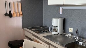 A compact kitchen with a stove, sink, and a coffee maker. There are wooden utensils hanging on the wall and a trash bin. - Nautillus 304 (Nieuwpoort)