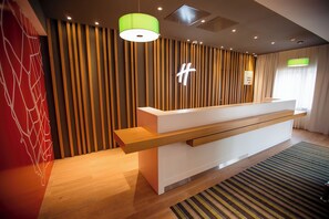A reception desk with a modern design, a wooden slat wall, and a green pendant light. - Holiday Inn Aktau - Seaside by IHG (Aktau)