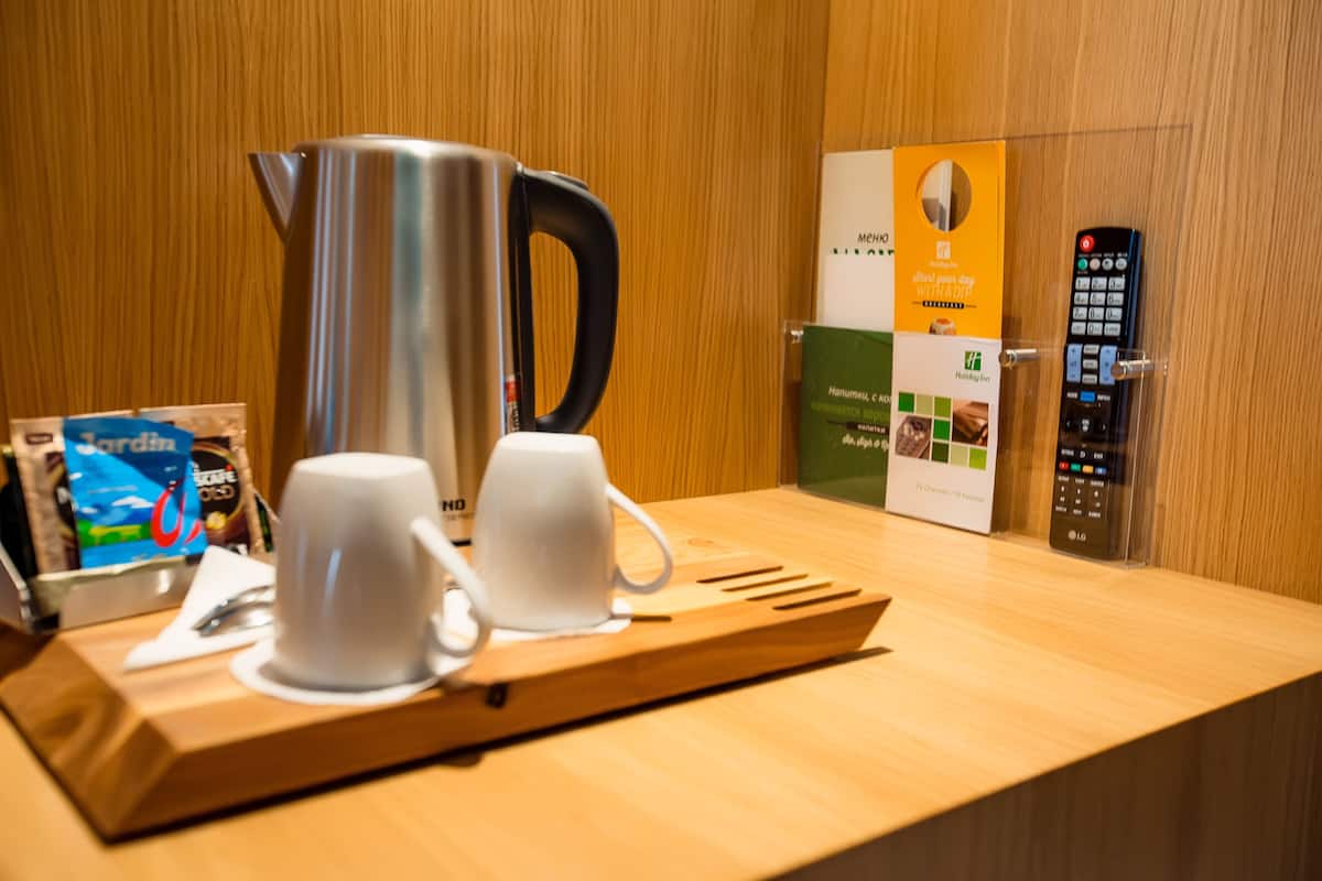 A wooden table with a coffee pot, two white cups, a tray, a remote control, and a sign with text.