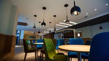 Un comedor moderno con sillas verdes y azules, mesas de madera e iluminación colgante.