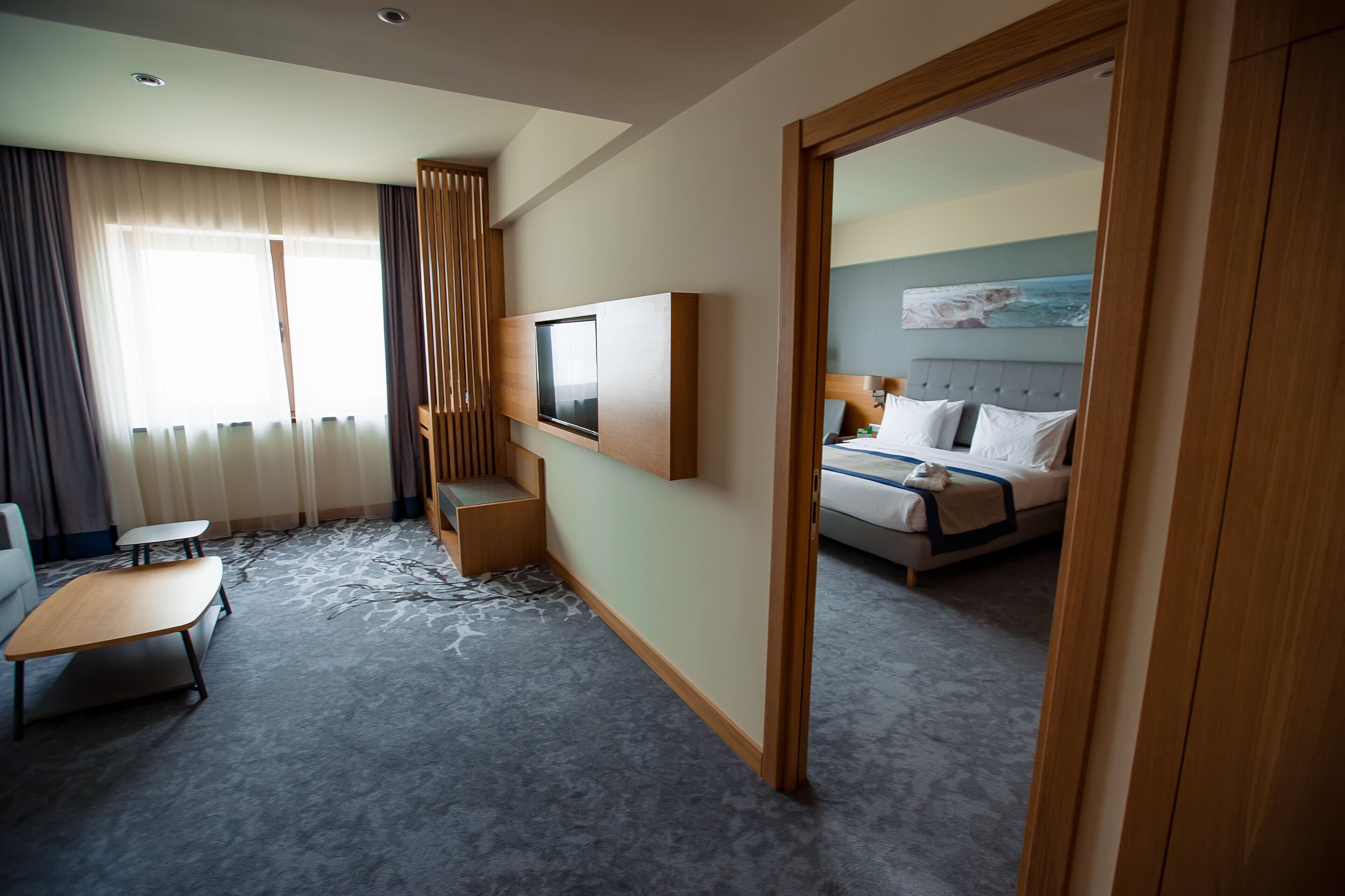 A hotel room with a bed, a desk, a chair, a TV, and a large window with curtains.