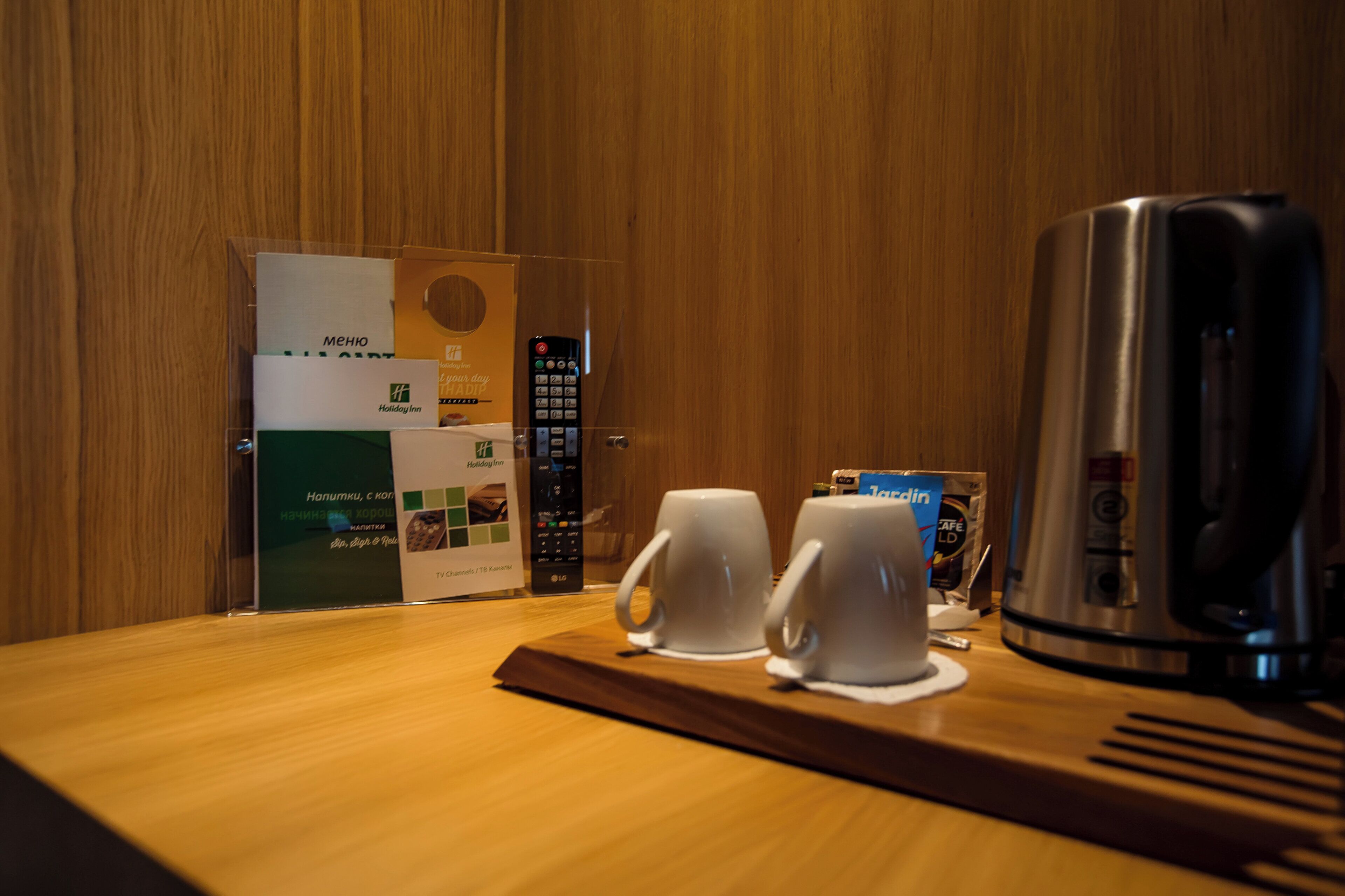 A hotel room with a wooden wall, a coffee maker, two white cups, and a remote control on a wooden tray.