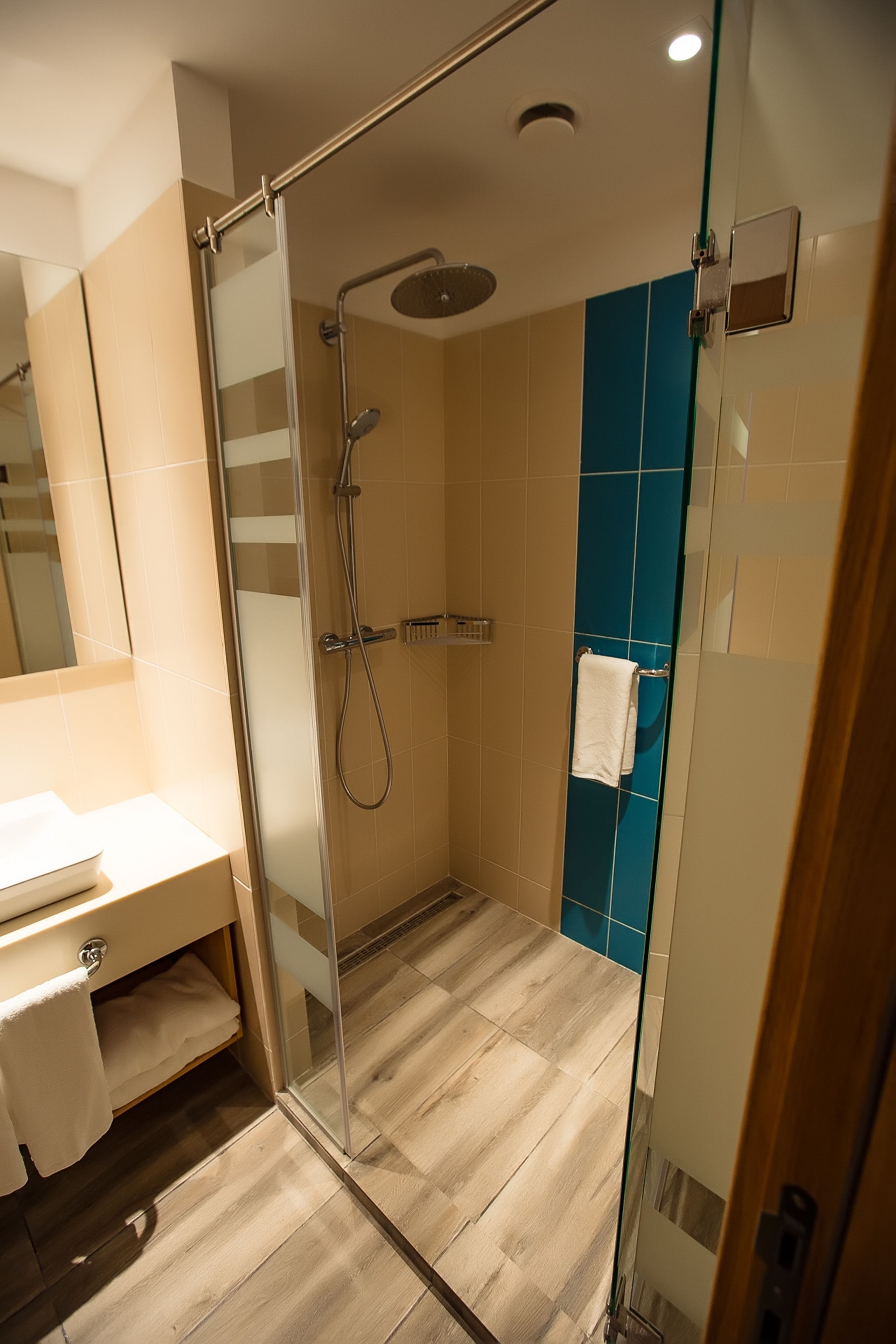 A modern bathroom with a glass shower enclosure, a white sink, and a blue accent wall.