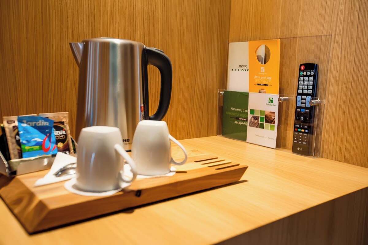 Un espace d’accueil d’hôtel avec un comptoir en bois, une cafetière, deux tasses blanches, une télécommande et des brochures d’information.