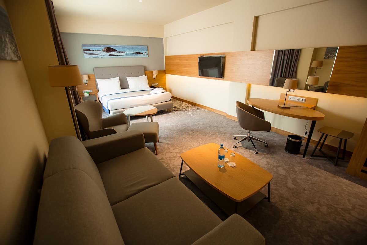 A hotel room with a bed, sofa, desk, and a TV.