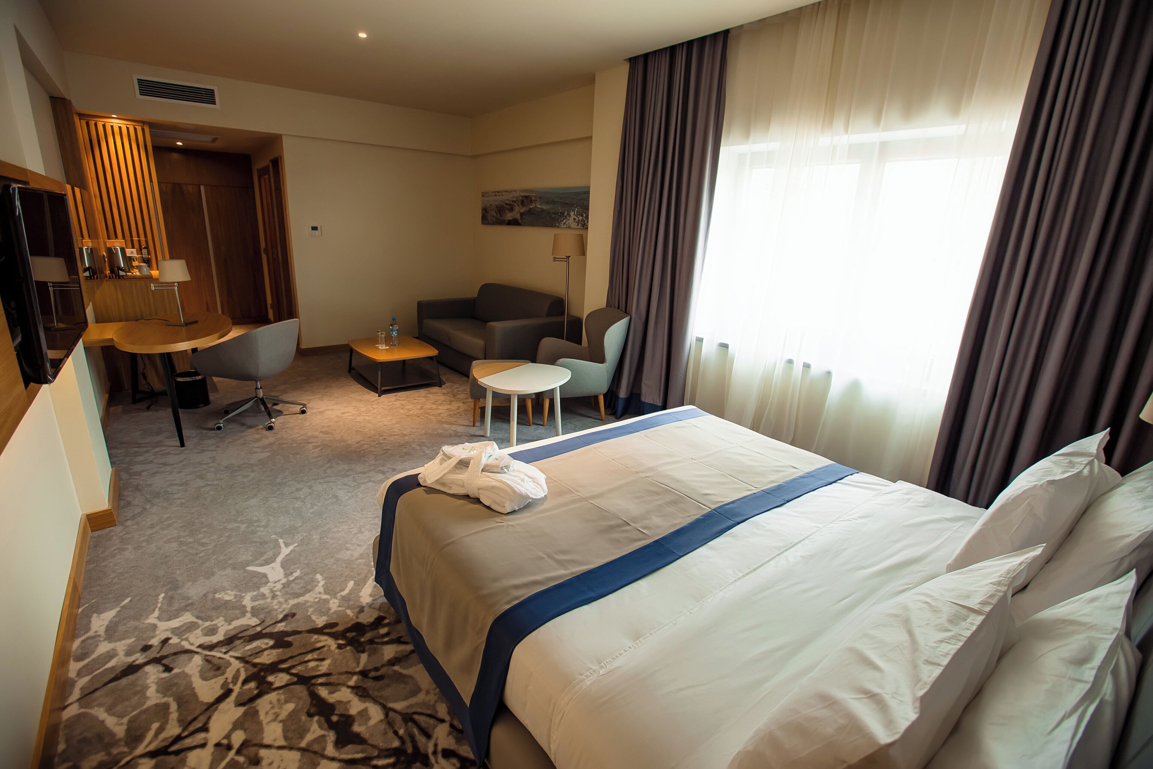 Una habitación de hotel con cama, escritorio, silla, sofá y ventana con cortinas.