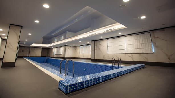 An indoor swimming pool with a blue tiled floor, surrounded by walls with marble-like patterns, and recessed ceiling lights. - Holiday Inn Aktau - Seaside by IHG (Aktau)