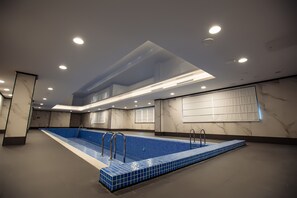 Una piscina interior con suelo de baldosas azules, rodeada de paredes con diseños similares al mármol y luces empotradas en el techo.