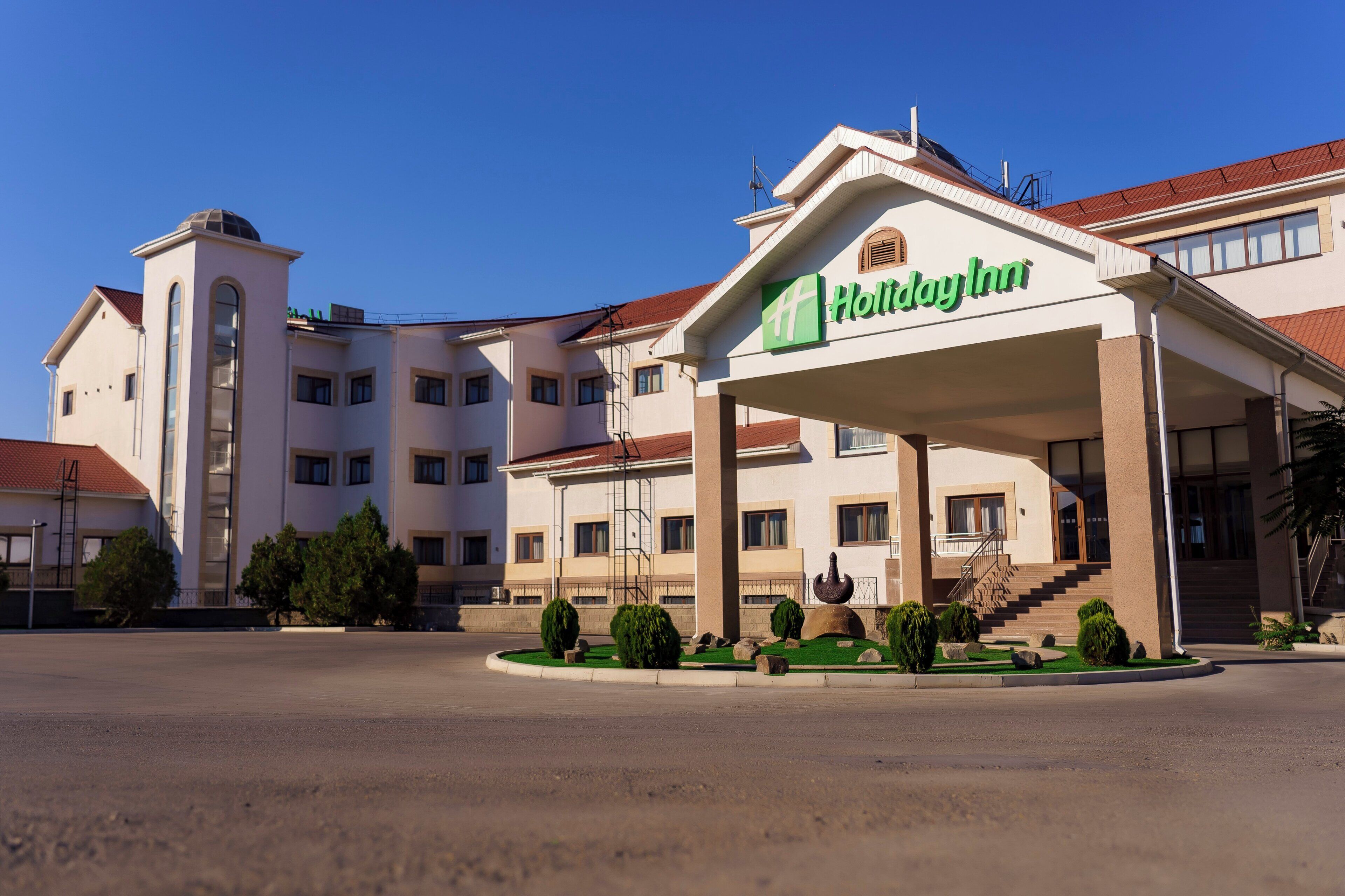 Um hotel Holiday Inn com entrada coberta, várias janelas e área de jardim ajardinada.
